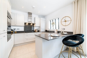 An open plan kitchen dining area with white cabinets and dark surfaces plus two high stalls next to the breakfast bar