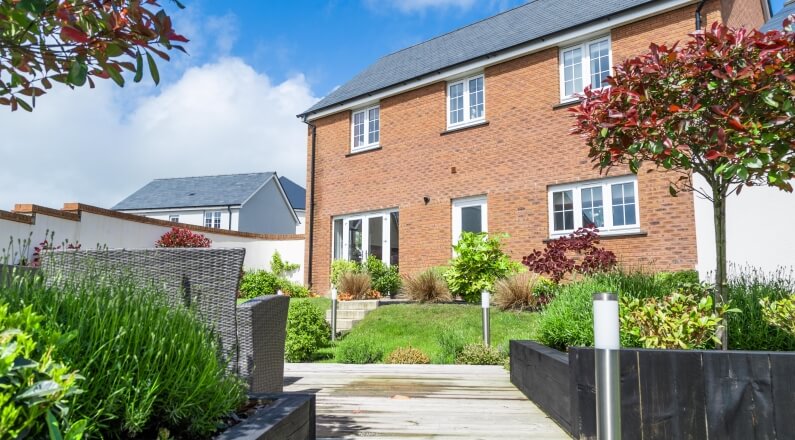 Rear garden with flower beds and the rear of a red brick house