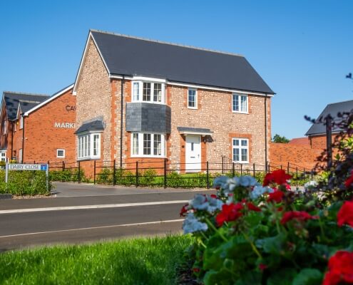 stone front house against bright blue sky with red and white flowers in foreground