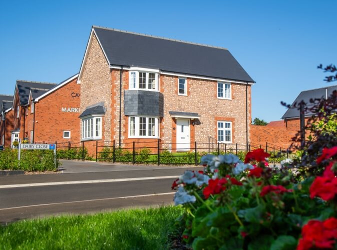 stone front house against bright blue sky with red and white flowers in foreground