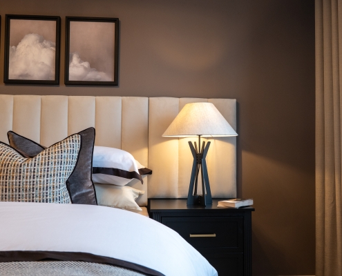 Beautifully made bed and bedside table with book and lamp.